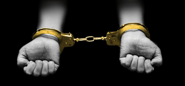 Hands restrained by gold-colored handcuffs against a black background